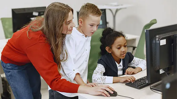 Image of instructor holding a mouse and two children behind a computer screen