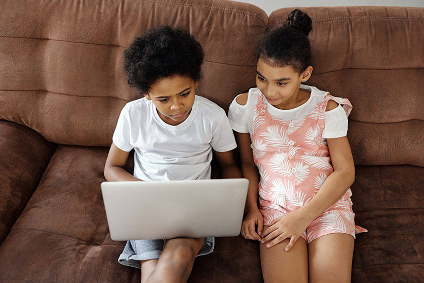 Two children using a laptop sitting on the couch