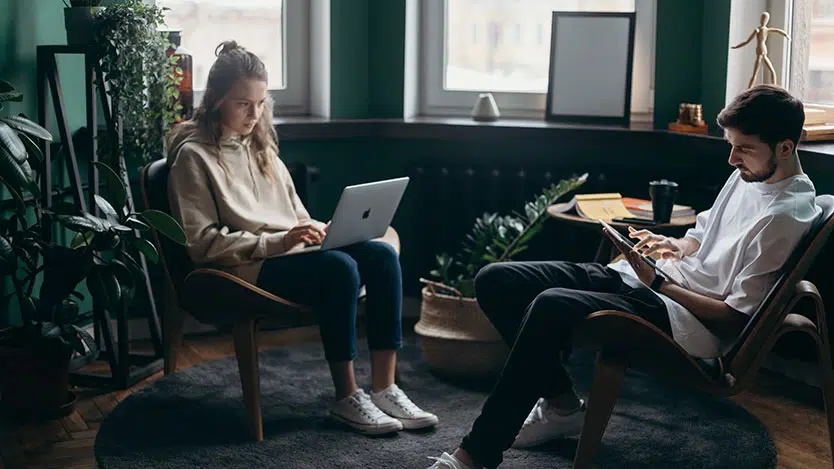 Guy and girl on a laptop and tablet in a living room, people using tech