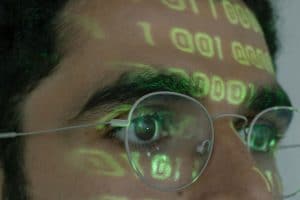 Man with glasses zoomed in, binary code reflected on forehead