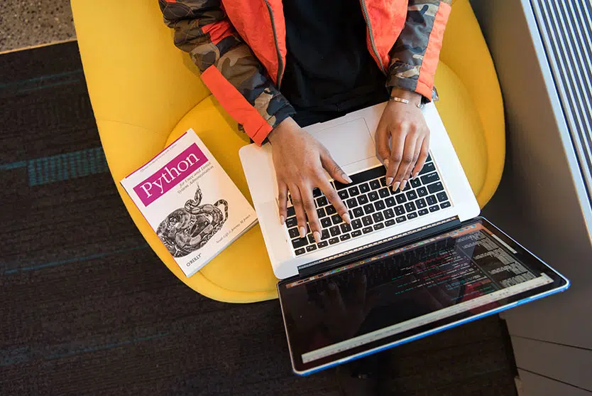 Woman at laptop, Python book of coding language on lap