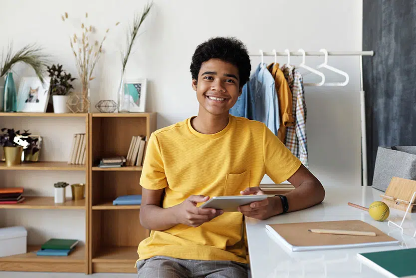 Kid smiling, holding a tablet at a desk