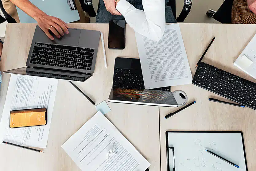 a desk with papers, laptops, and people, seen from above