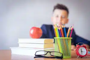 faded student behind a desk, with a book, apple, glasses in focus