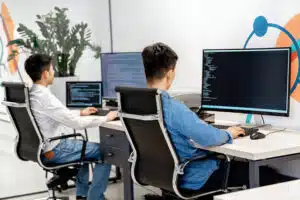 two guys programming on a desktop computer, seated side by side