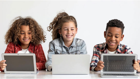 Three children sitting at a desktop behind laptops smiling