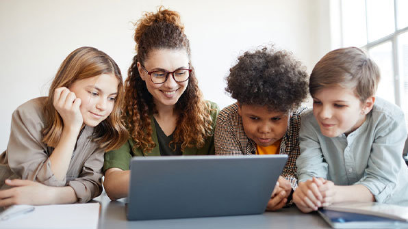 Portrait of smiling female teacher using computer with diverse group of children