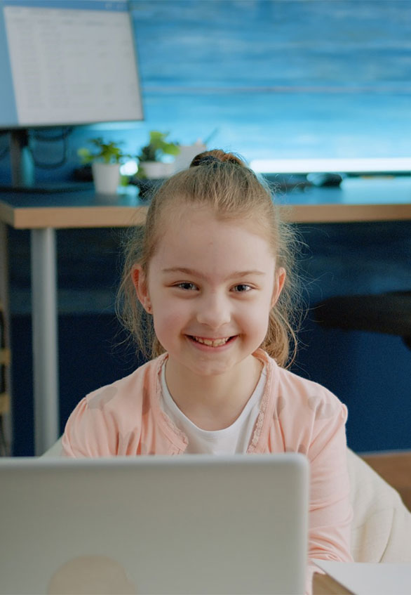 Portrait of young girl smiling and sitting behind laptop at home