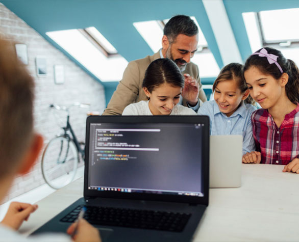 Four children and teacher at a desk smiling looking at laptop with code on  the screen