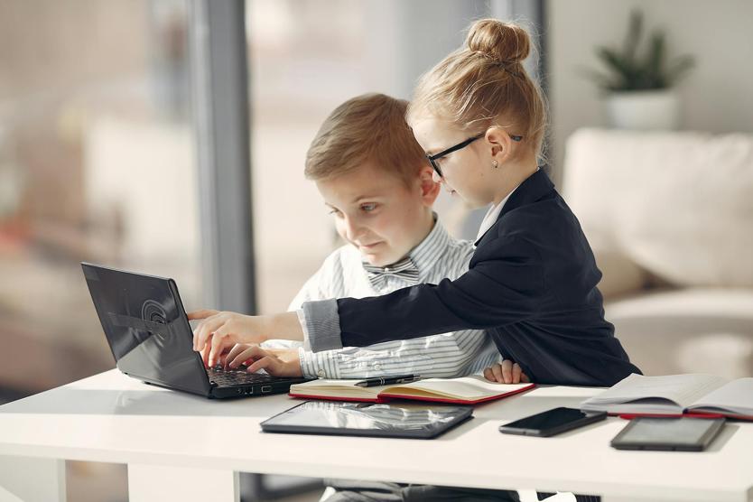 Two kids at a table looking at a laptop