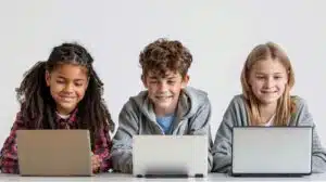 Three children sitting at a desk with laptops smiling